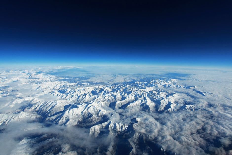 Stunning bird's eye view of snow-covered mountains beneath a clear blue sky.